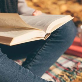 Mabon: Meanings and a Quick History 19 A person enjoying a peaceful autumn afternoon reading a book on occult themes, surrounded by fallen leaves, with a hot beverage nearby.