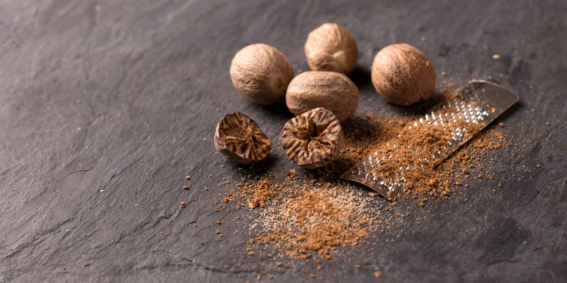 Whole nutmegs beside freshly grated nutmeg on a dark slate surface evoke a metaphysical ambiance.