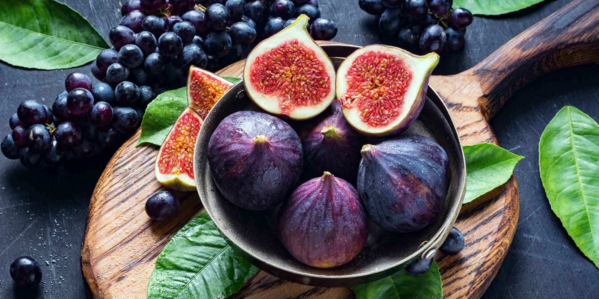 A bowl of figs surrounded by fig leaves on a wooden cutting board