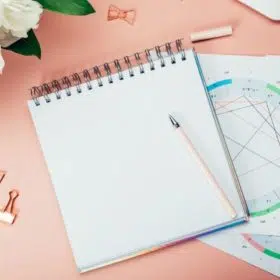 a notebook on astrological charts on a pink table