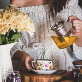a woman pouring tea from a glass tea pot into a teacup