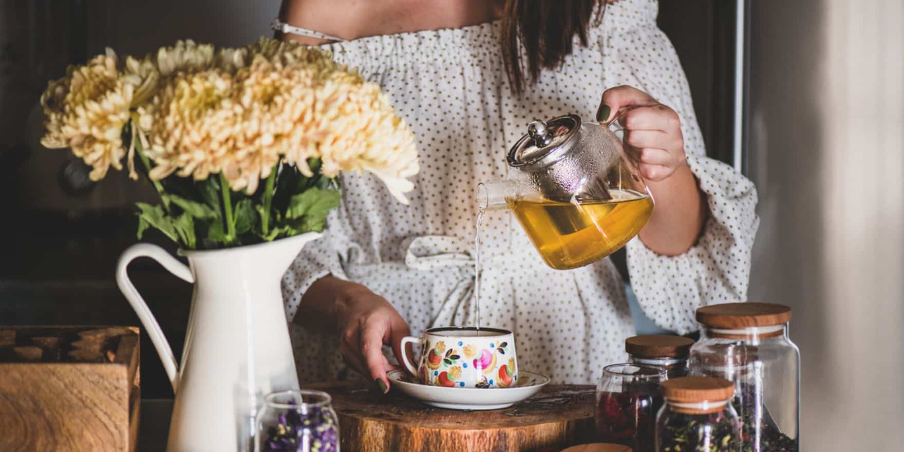 a woman pouring tea from a glass tea pot into a teacup