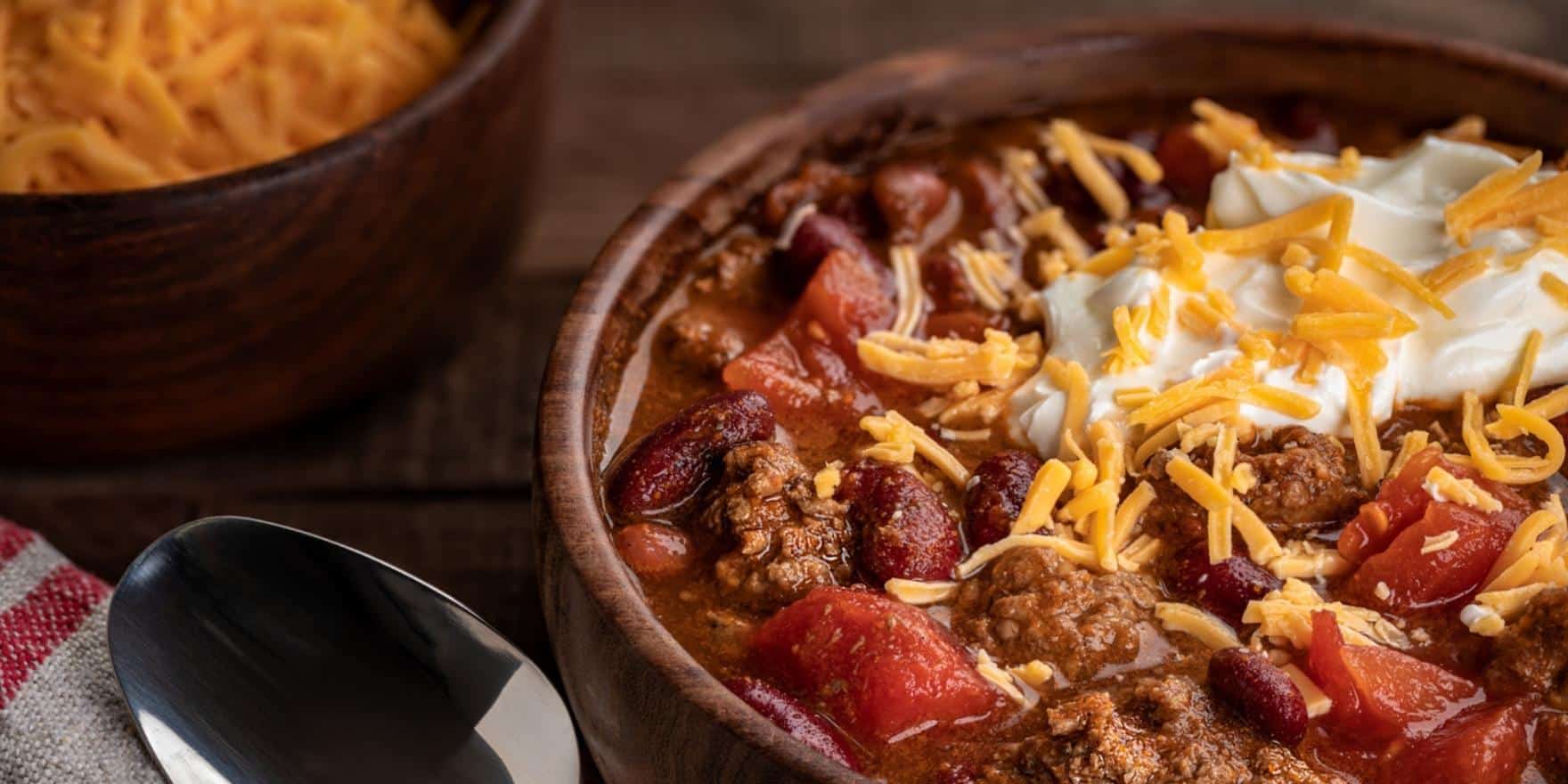 an image of chili in a bowl with sour cream and cheddar cheese on top