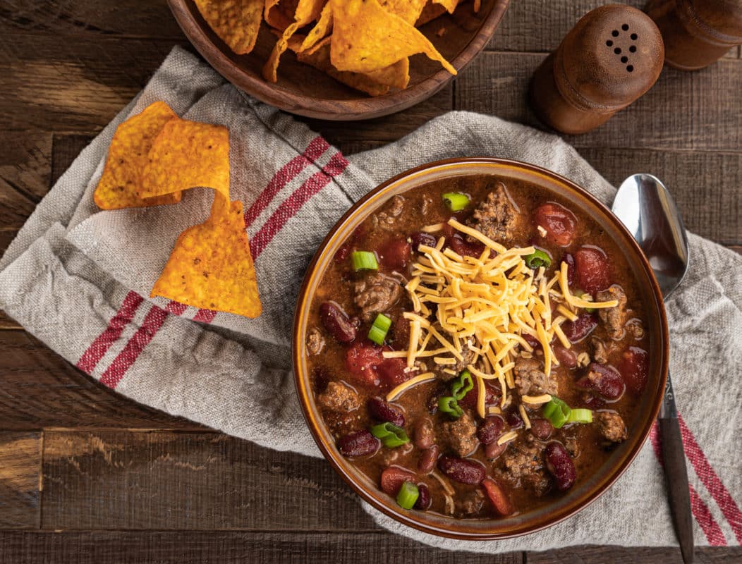 A bowl of chili with shredded cheddar cheese and tortilla chips.