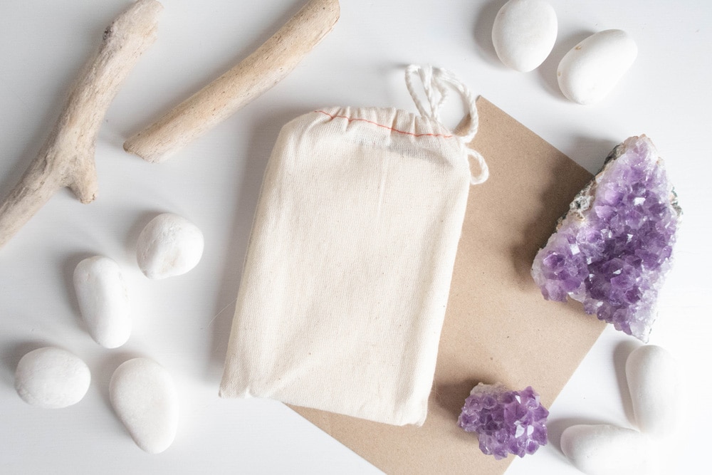 A linen bag next to amethyst clusters , white stones, and wooden wands