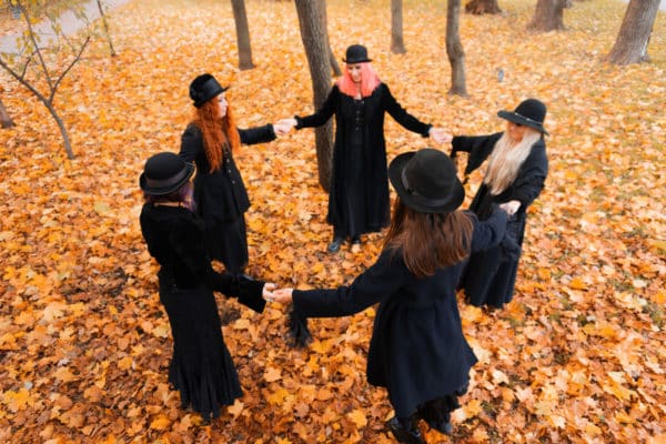a coven of witches in a circle surrounded by autumn leaves