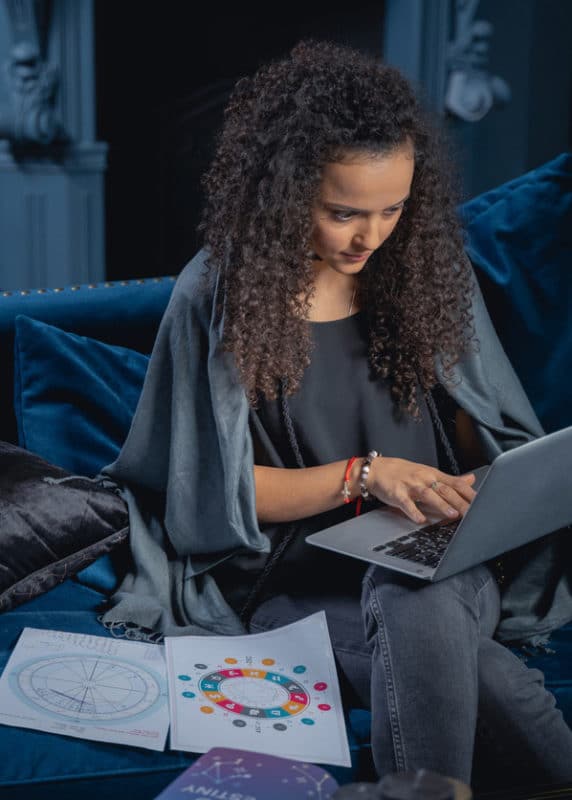 mixed race woman researching on her computer with astrological birth charts next to her