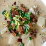 A bowl of creamy white clam chowder with bacon on top