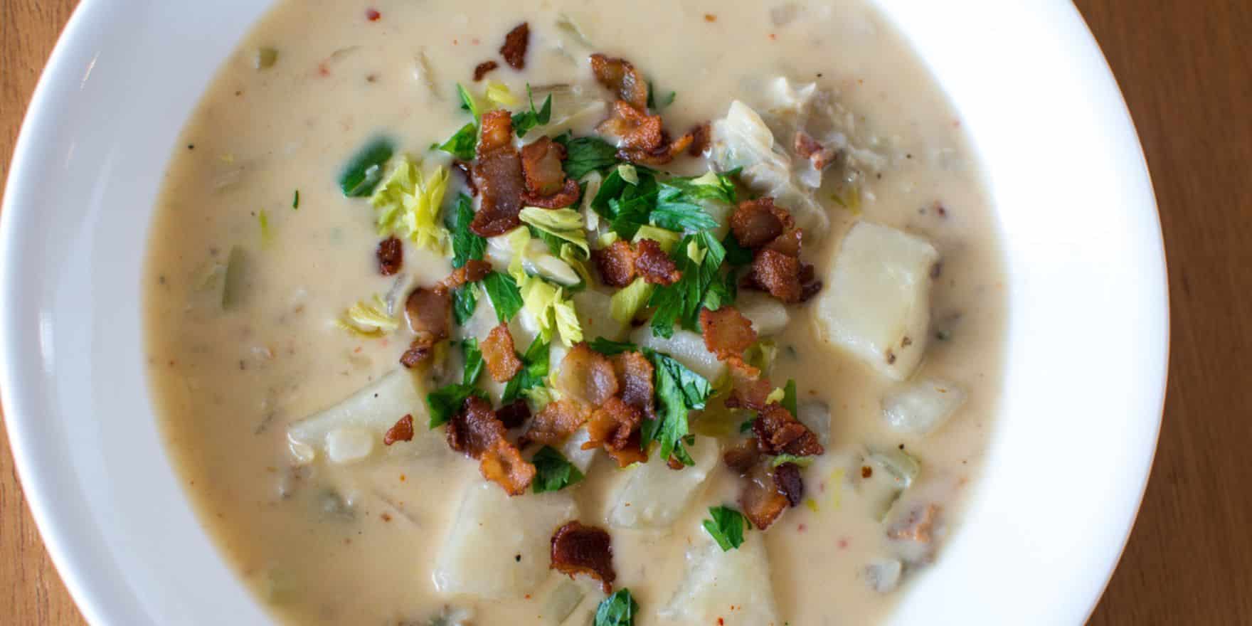 A bowl of creamy white clam chowder with bacon on top