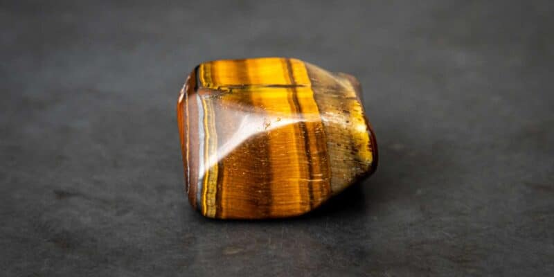 Magical Properties of Tiger's Eye | How to Use Tiger's Eye in Spells 8 A banded brown fiberoptic crystal on a grey table