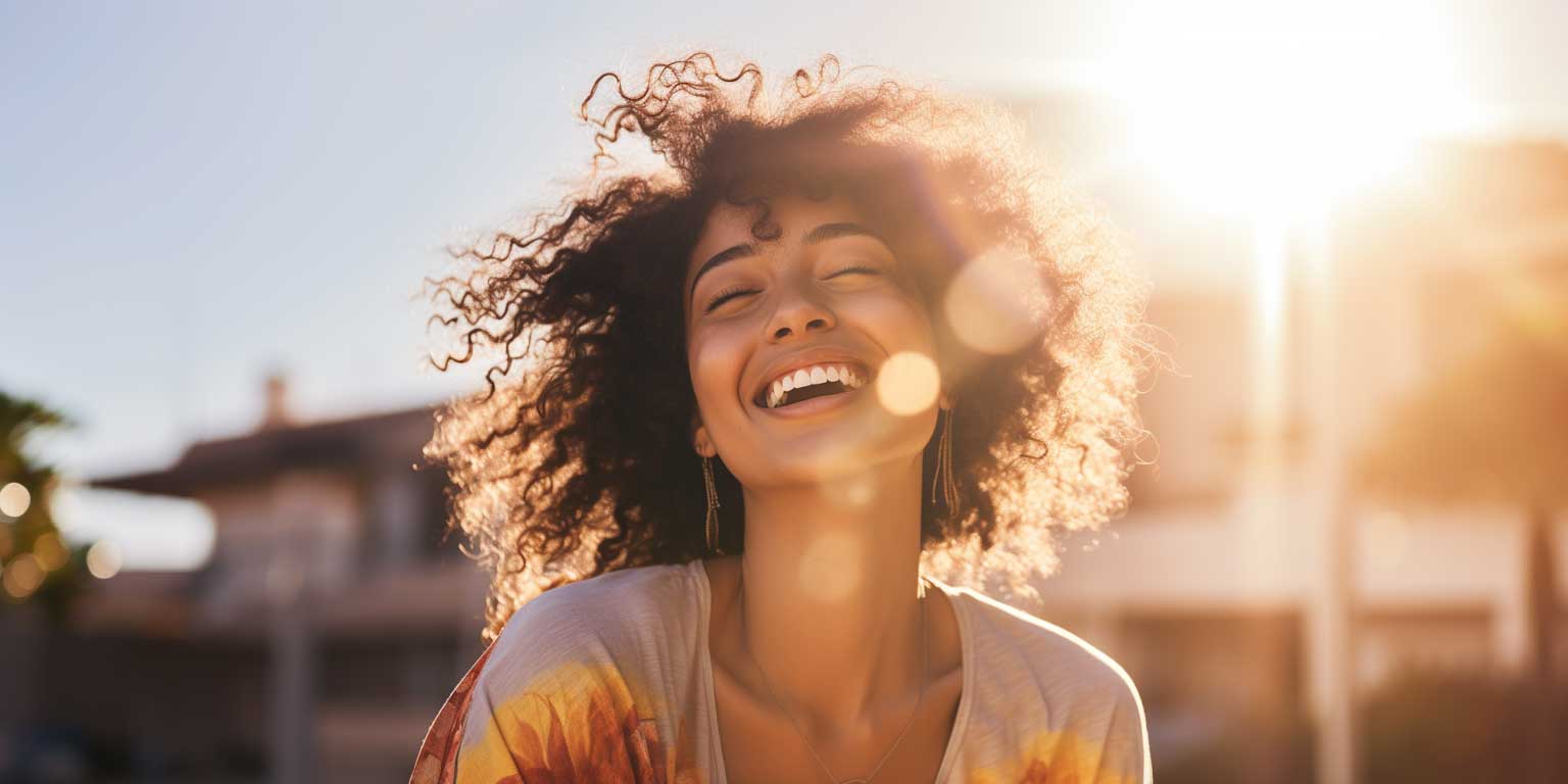 Woman with curly hair laughing in sunlight, raising vibration.