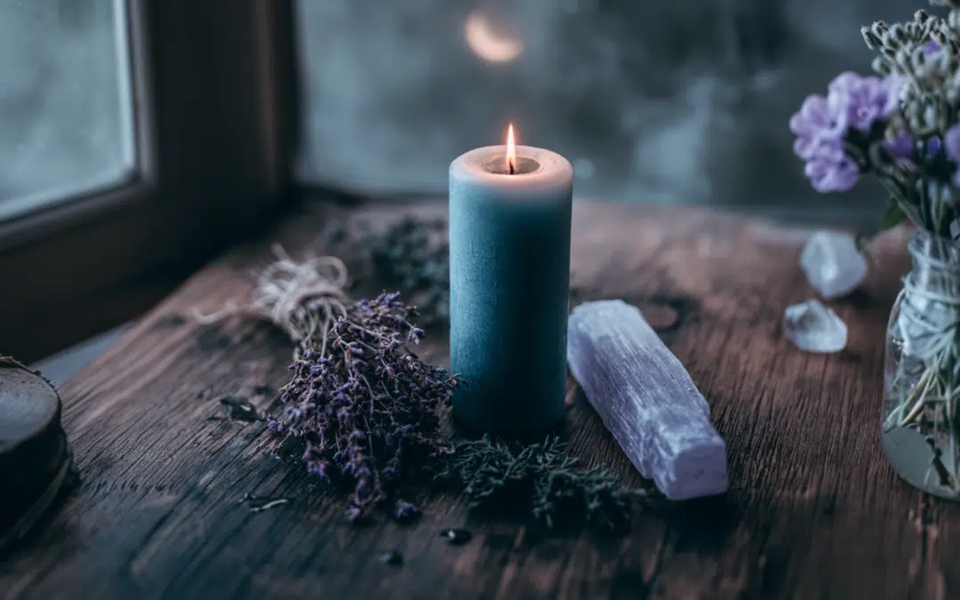 A blue pillar candle, dried lavender flowers, and a selenite stick arranged on a dark altar surface for a sadness working.