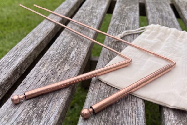 Copper dowsing rods Plentiful Earth | Global Spirituality Pair of copper dowsing rods with sleeve handles and ball ends on a wooden garden bench