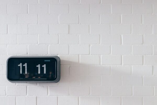 1111 angel number Plentiful Earth | Global Spirituality A black digital flip clock reading 11:11 on a white brick wall