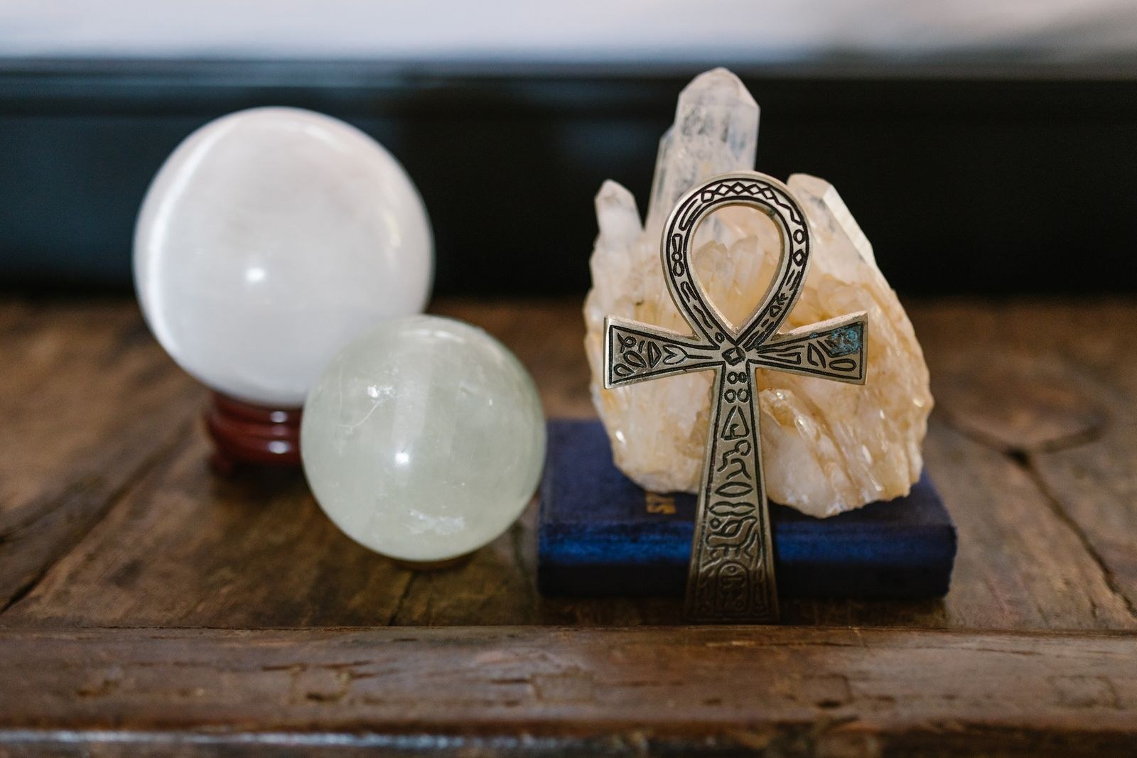 A metal ankh standing on a wooden table beside two clear crystal spheres and a quartz point