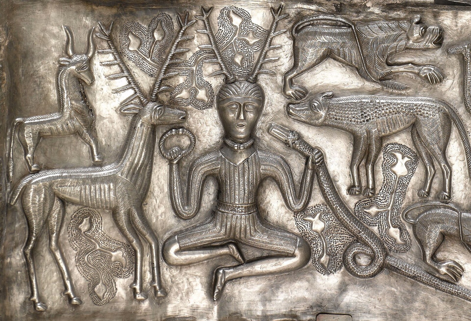 Antlered figure on the Gundestrup cauldron Plentiful Earth | Global Spirituality Silver plate from the Gundestrup cauldron showing an antlered figure seated cross-legged, holding a torc and a ram-horned serpent among animals