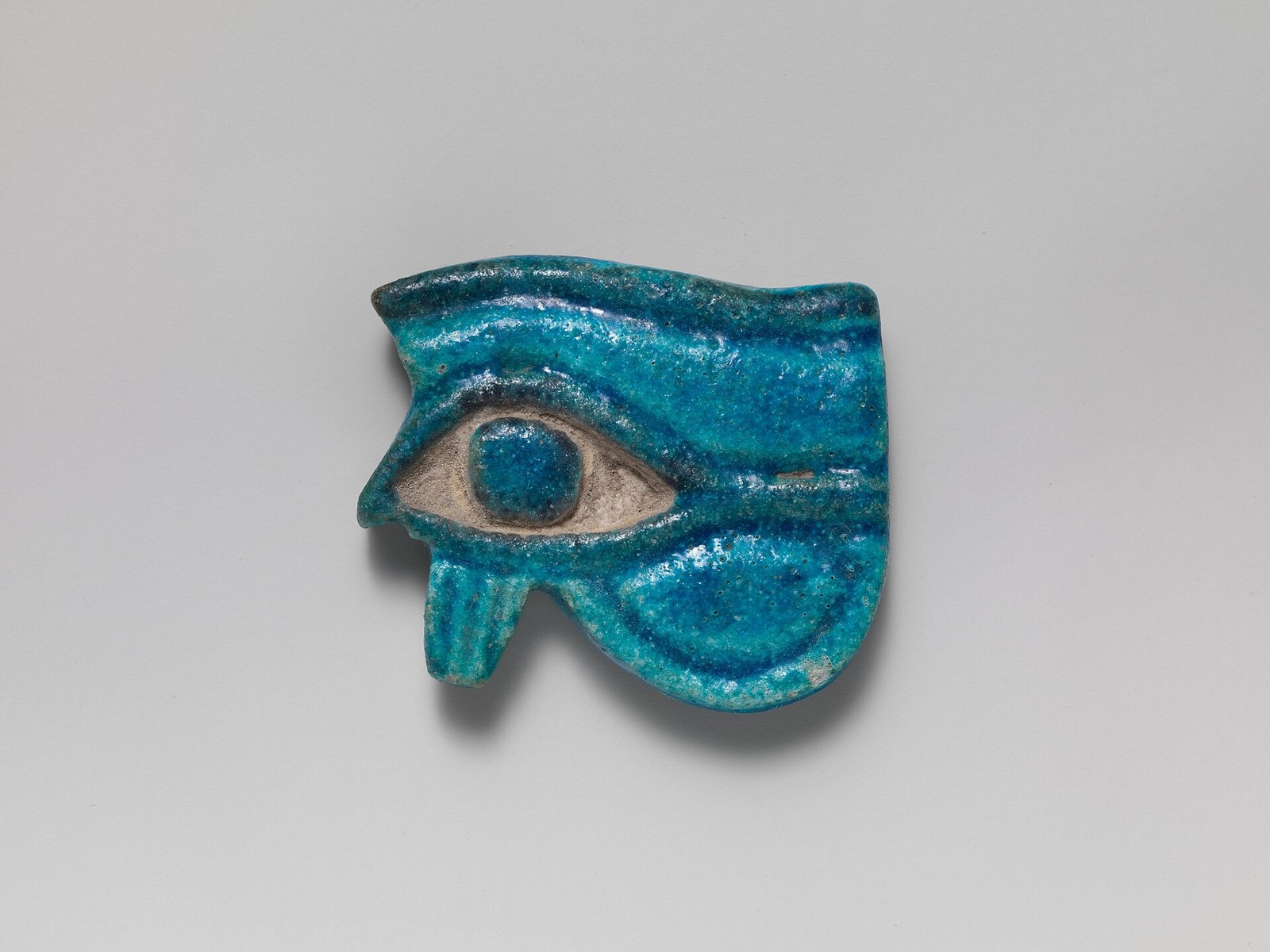 A bright blue faience Eye of Horus amulet showing a stylized eye with the falcon markings beneath it