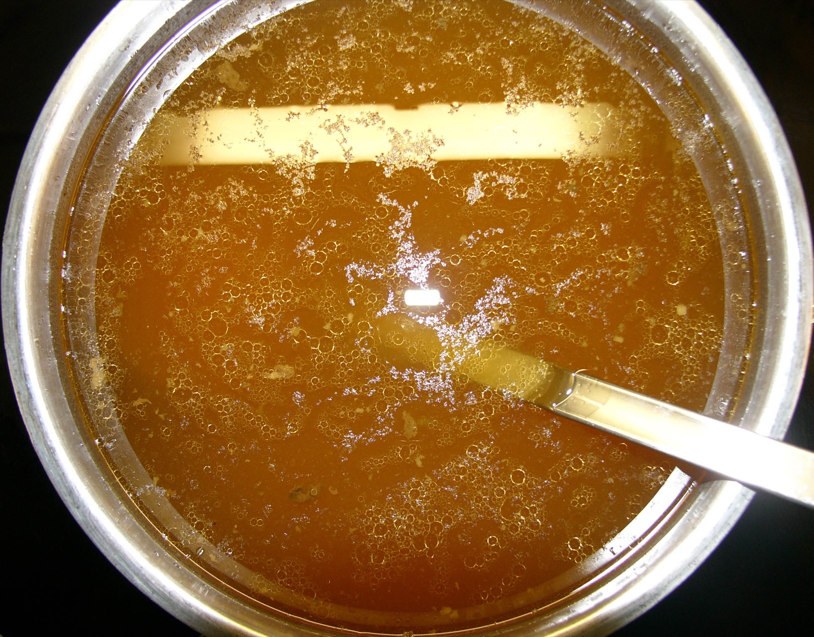 Rich amber homemade bone broth in a metal pot with a spoon