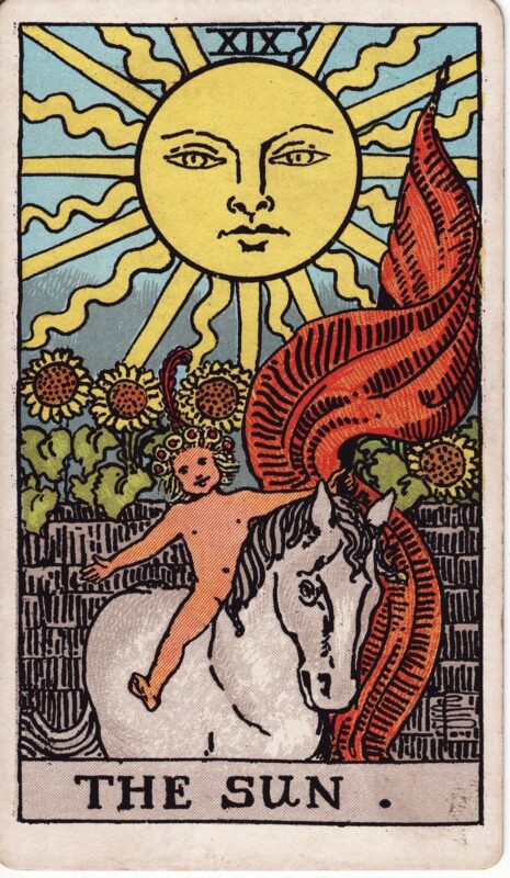 The Sun RiderWaiteSmith 1909 Plentiful Earth | Global Spirituality The Sun tarot card from the 1909 Rider-Waite-Smith deck: a large smiling sun with straight and wavy rays shines over a gray stone wall lined with sunflowers, while a child wearing a wreath rides a white horse with arms spread wide, beside a flowing red banner