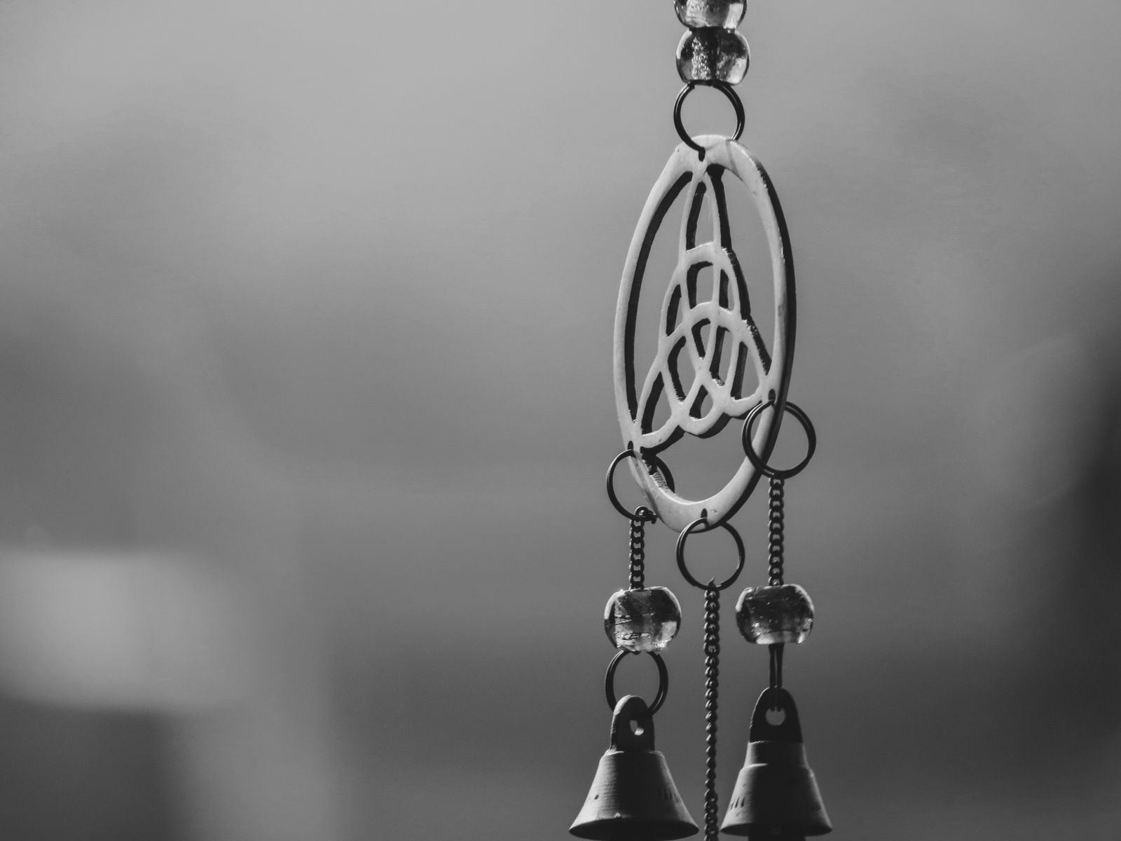 Black-and-white close-up of a hanging metal wind chime shaped like a triquetra inside a circle, with small bells below