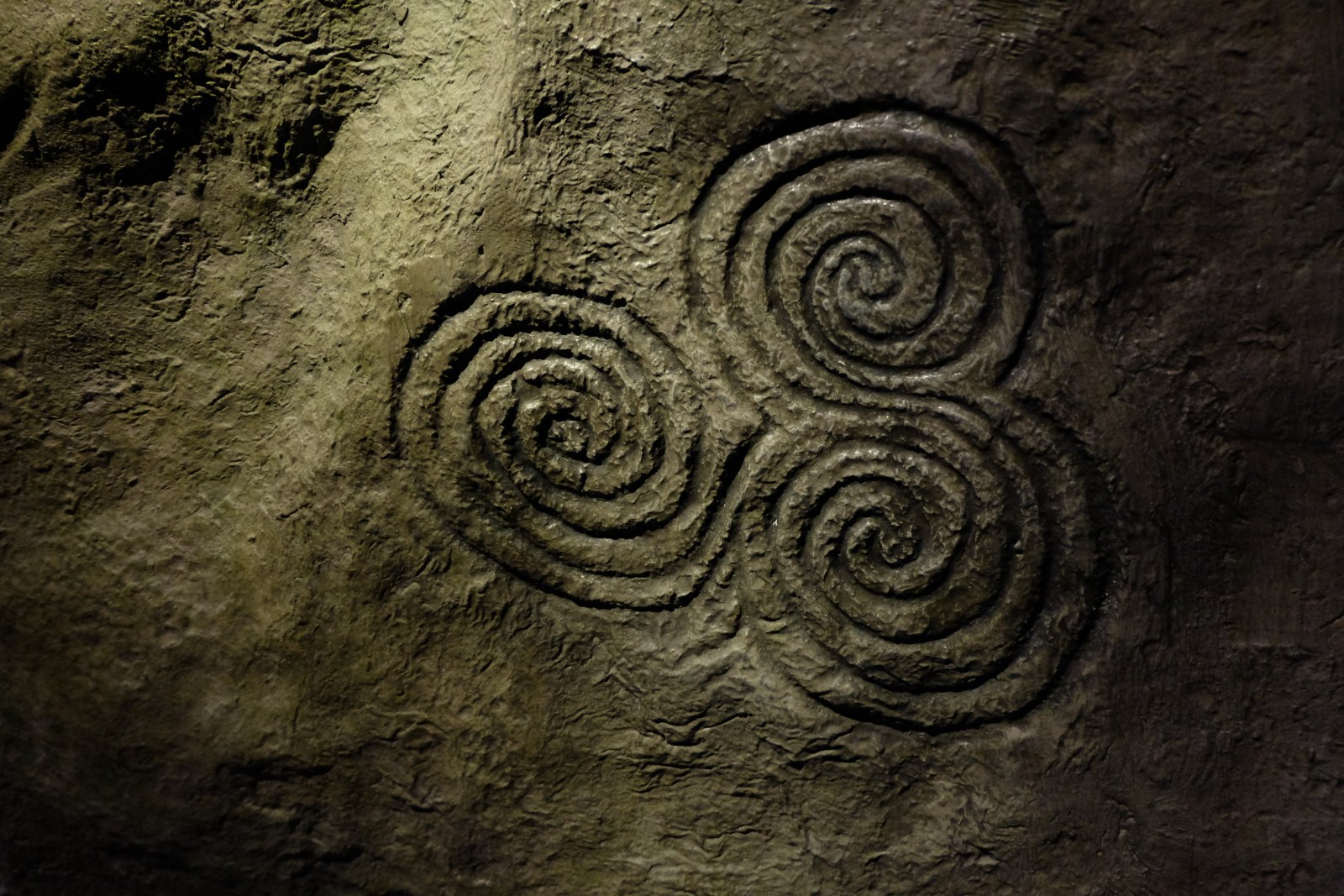 Three joined spirals carved into dark stone at Newgrange, Ireland