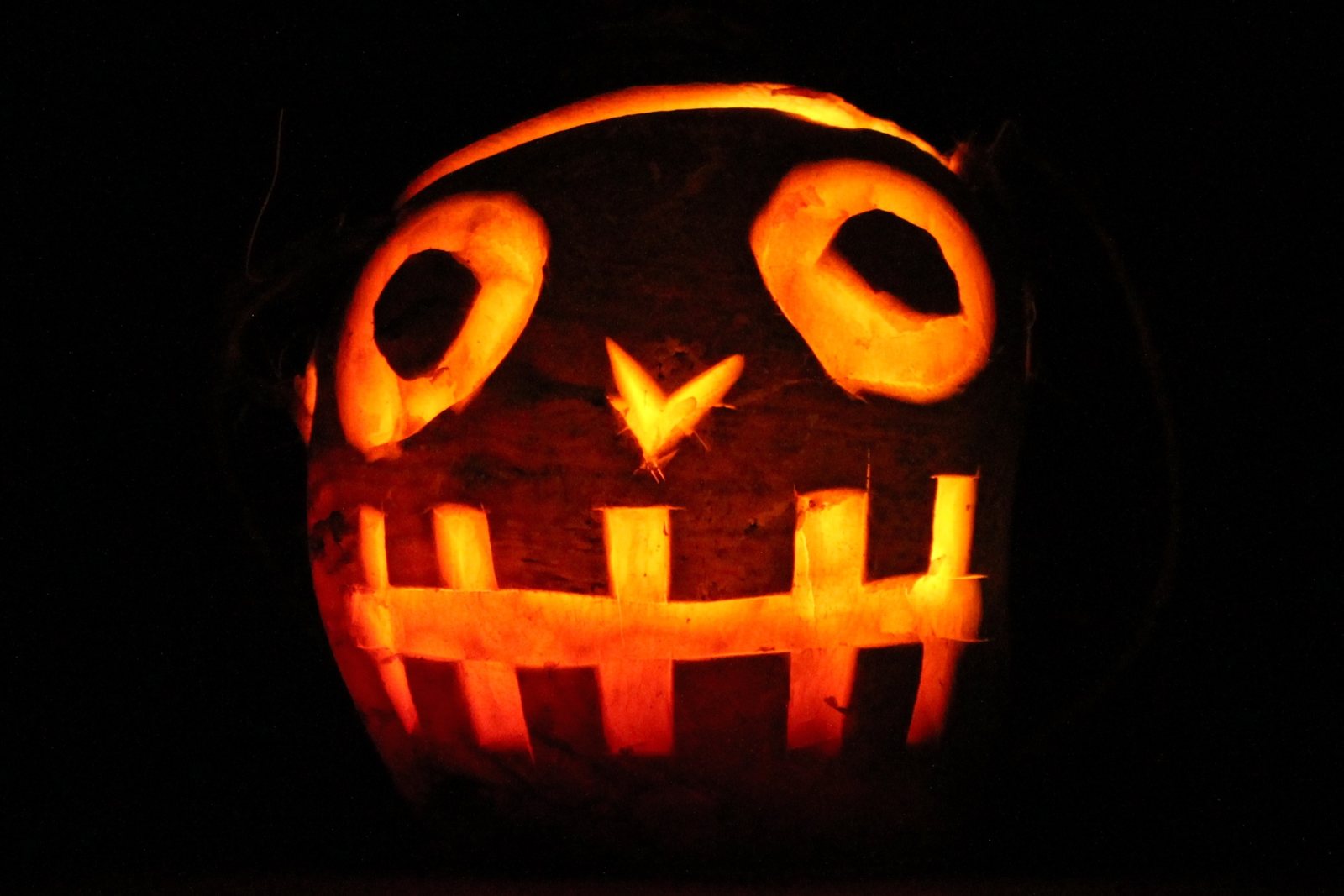 A turnip jack-o'-lantern glowing orange in the dark, carved with round eyes, a small nose, and a wide grin of square teeth.