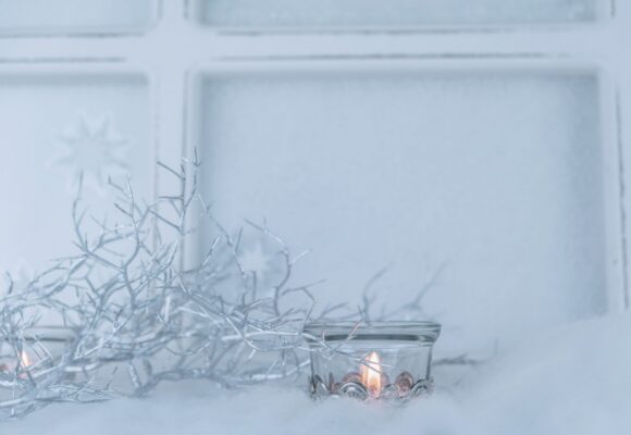 Winter witchcraft candles and frost Plentiful Earth | Global Spirituality Lit candles and frosted silver twigs against a snowy window.